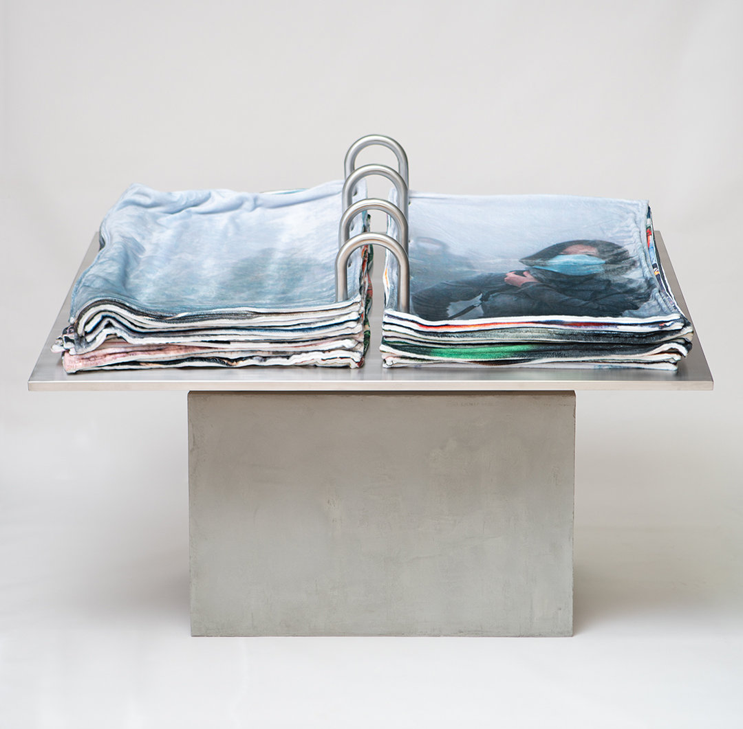 Book of Dread, 2020. The Book of Dread is a continuation of the ‘Security Blanket’ project begun in 2015. Each blanket image is presented across the fold of a 67 x 45 inch stainless steel ‘book.’ The viewer flips the pages, encountering simultaneously the comforting softness of the blankets and their disturbing depictions. Courtesy of the artist.