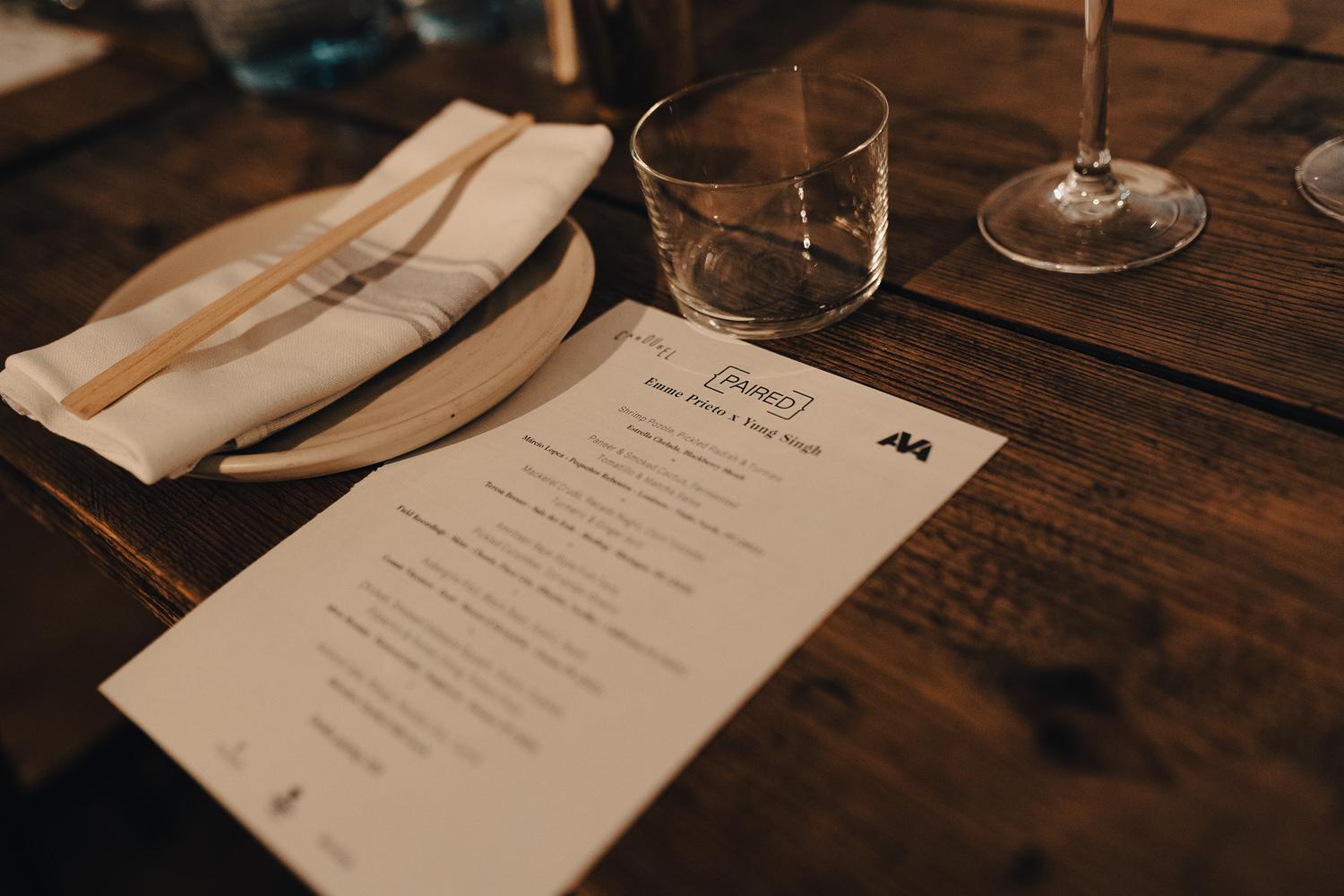 Close-up of a Paired menu featuring Emme Prieto × Yung Singh with AVA and Carousel London branding beside tableware and chopsticks.