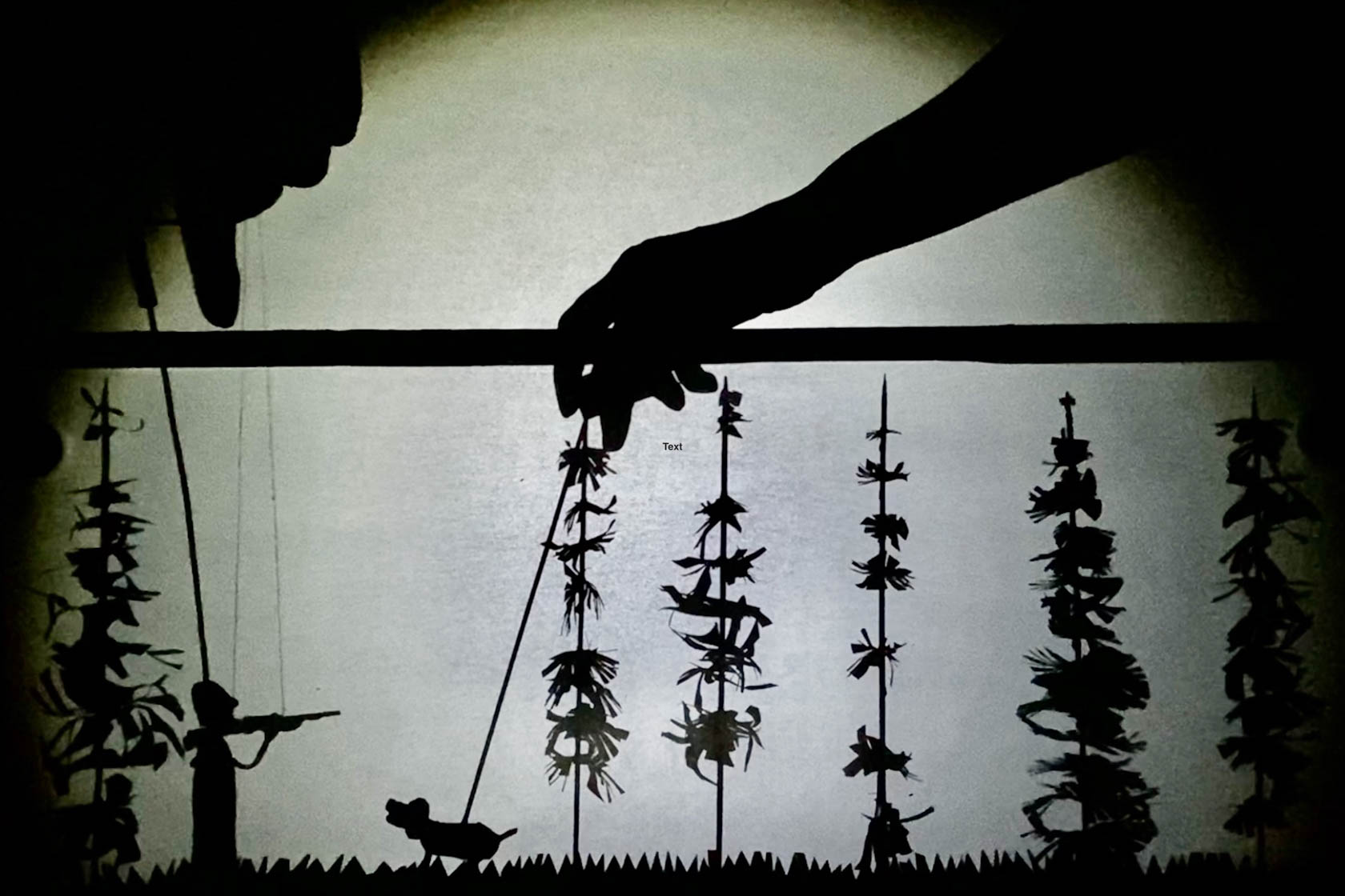 Shadow puppet scene of a person holding up a rifle in a forest with a dog.