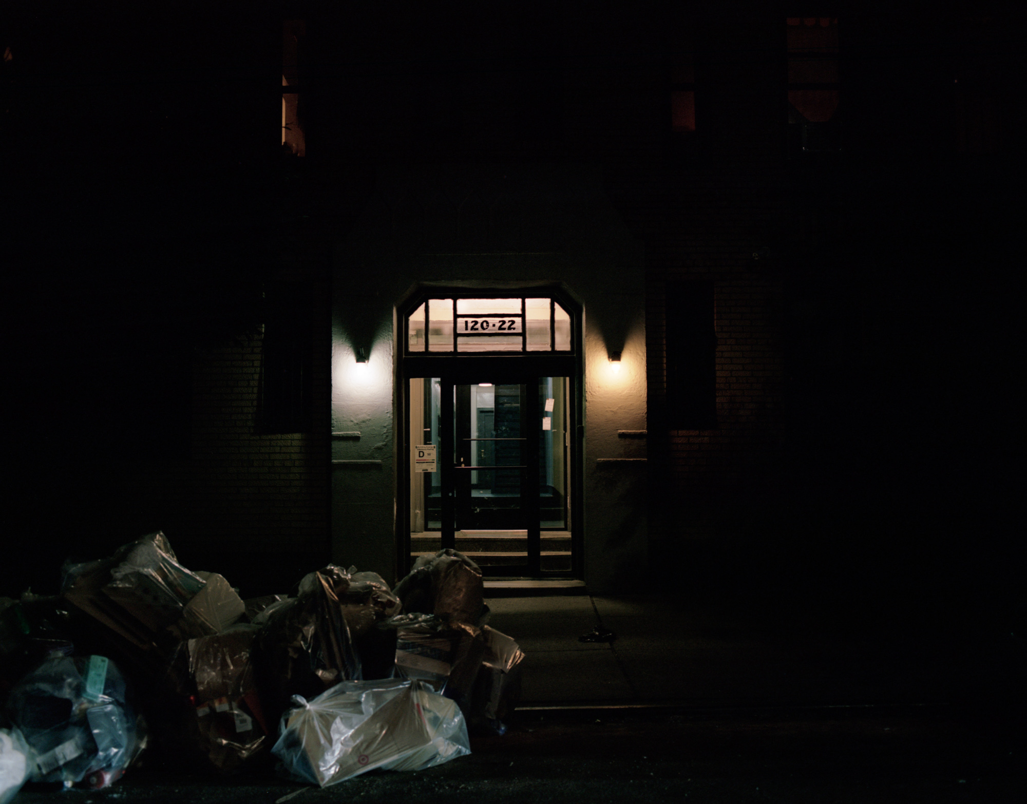 Even with the trash and recycling at the curb, the fa&ccedil;ade of 120 Odell Clark Place appears cinematic with the night&rsquo;s shadow masking its flaws and the different-colored front lights shining as our beacon of home.