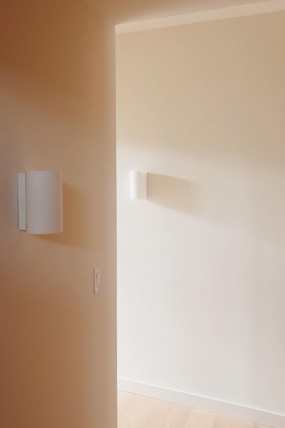 Interior photo of the Brant Beach renovation, highlighting two modern white cylindrical sconce lights installed on a warm-toned wall in a hallway.