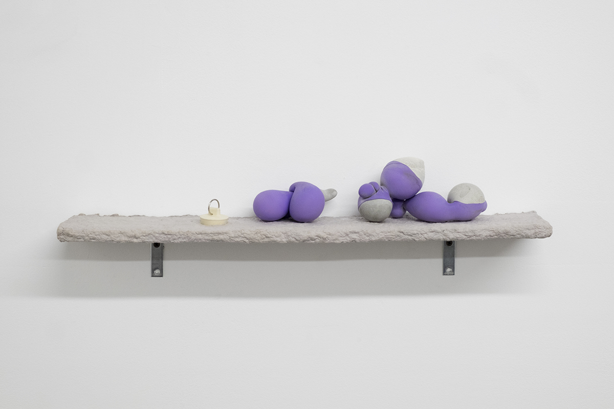 3 Hand-sized rounded concrete forms coated in bright lavender latex sit on a gray paper pulp coated shelf on a white wall. The shelf is punctuated with a rubber drain stopper.
