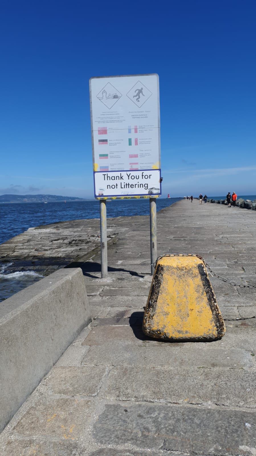 A concrete pathway along the river. A sign says Thank You For Not Littering