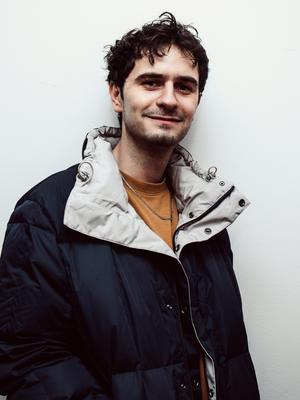 Charley McDermott-Edwards, Designer at UP! Productions, wearing a navy puffer jacket and mustard jumper.