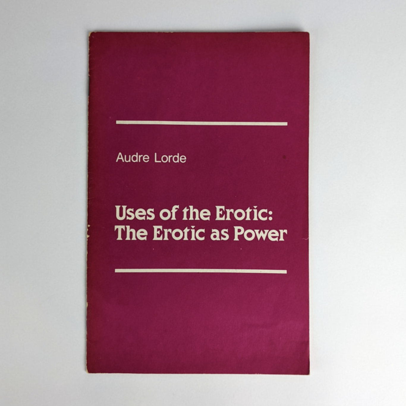 A redish zine sits on a grey table top. The title reads: Uses of the Erotic: The Erotic as Power by Audre Lorde.
