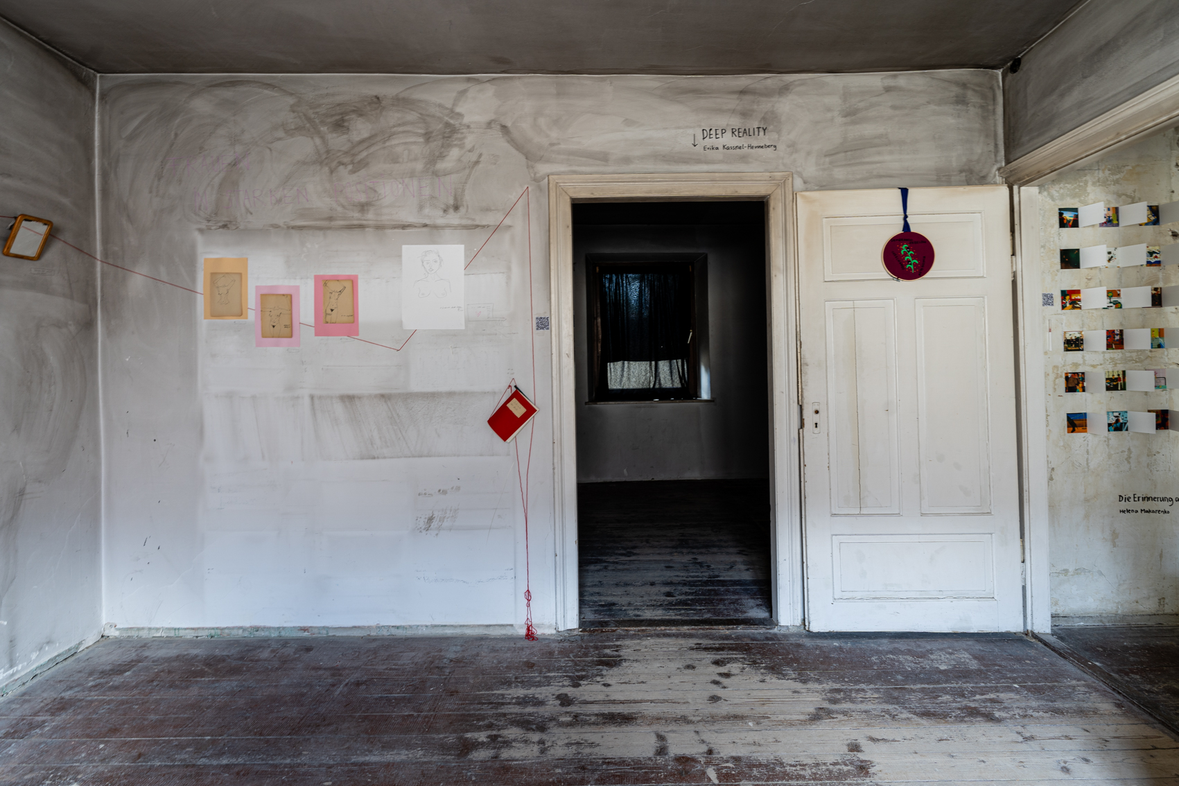 Bild 1 zu ImmerWiederNeuBeginnerin: Im Raum mit Blick auf den Durchgang zum Raum Deep Reality. Links der Tür hängen Zeichnungen von Körpern an einer Wand, die graue Schlieren hat. Die Zeichnungen sind mit einem roten Faden verbunden.