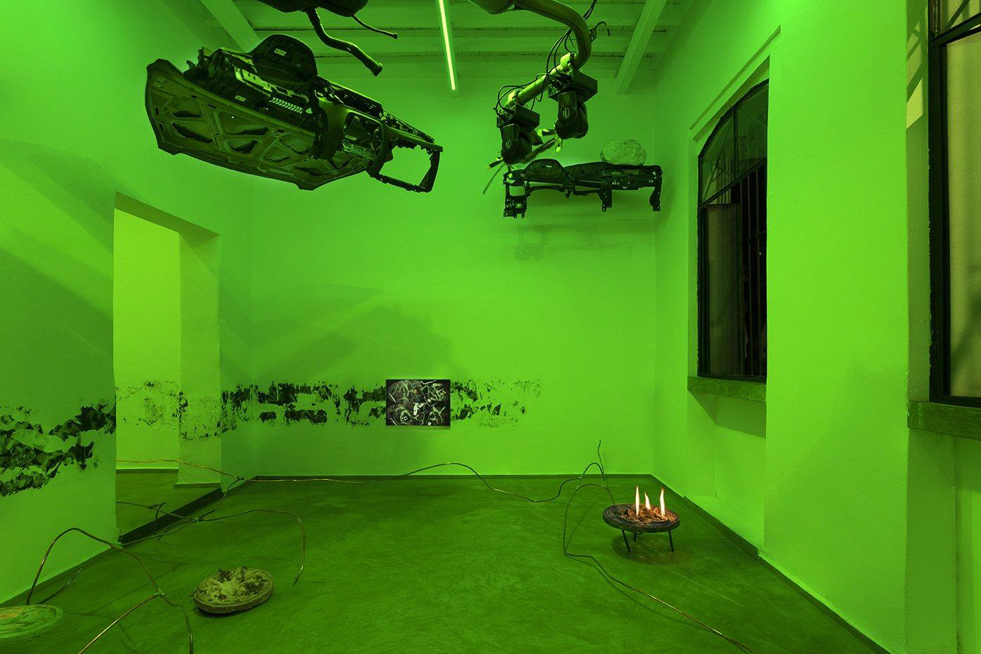 Rodrigo Red Sandoval, Towards a Lower Sky, 2023, fire, gas, crashed car parts, copper pipes, metal, wood, bronze, concrete, ceramic, weeds, pigeon feathers, robotic lights, jesmonite, screen bracket, lighter, beer cans, digital prints, dimensions variable. © Rodrigo Red Sandoval. 