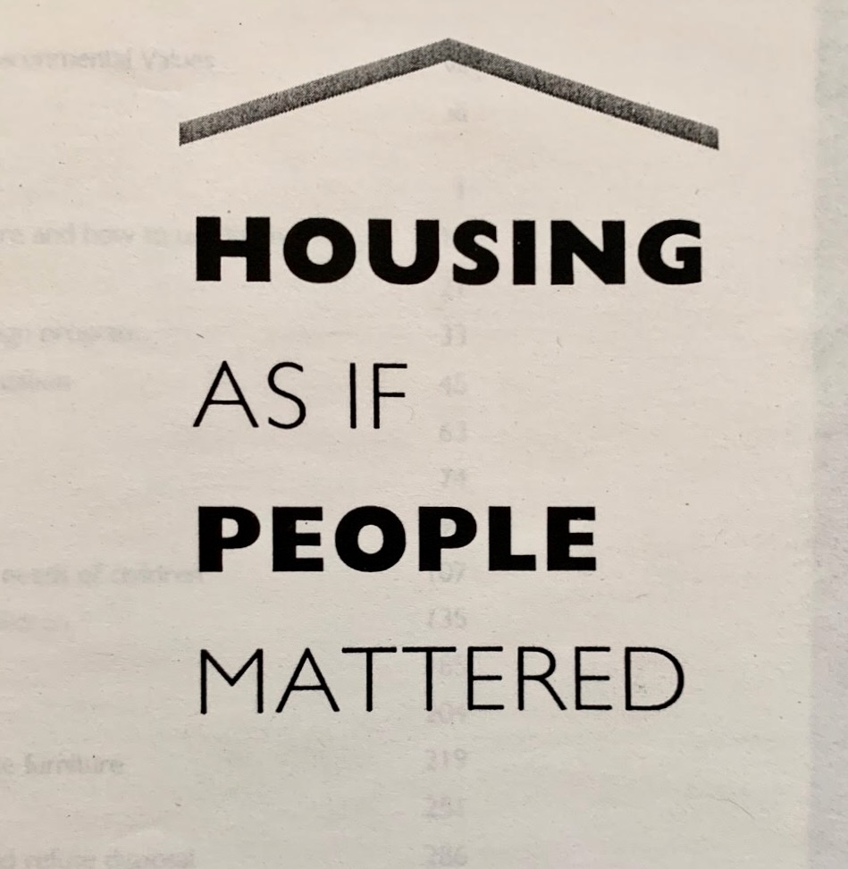 A poster with black text that reads Housing as if People Mattered.