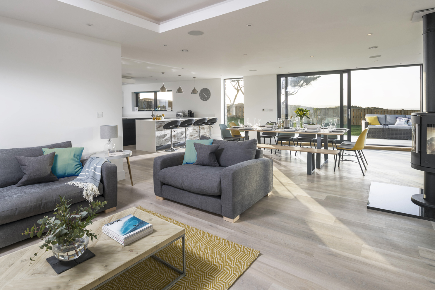 Modern kitchen, dining room and lounge. Grey, mustard yellow and teal colour palette. Large glazed windows and natural light. 