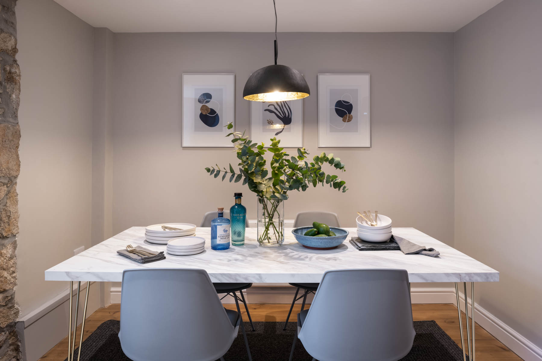 Front perspective of marble table with grey chairs. Dark pendant above and abstract art on wall.