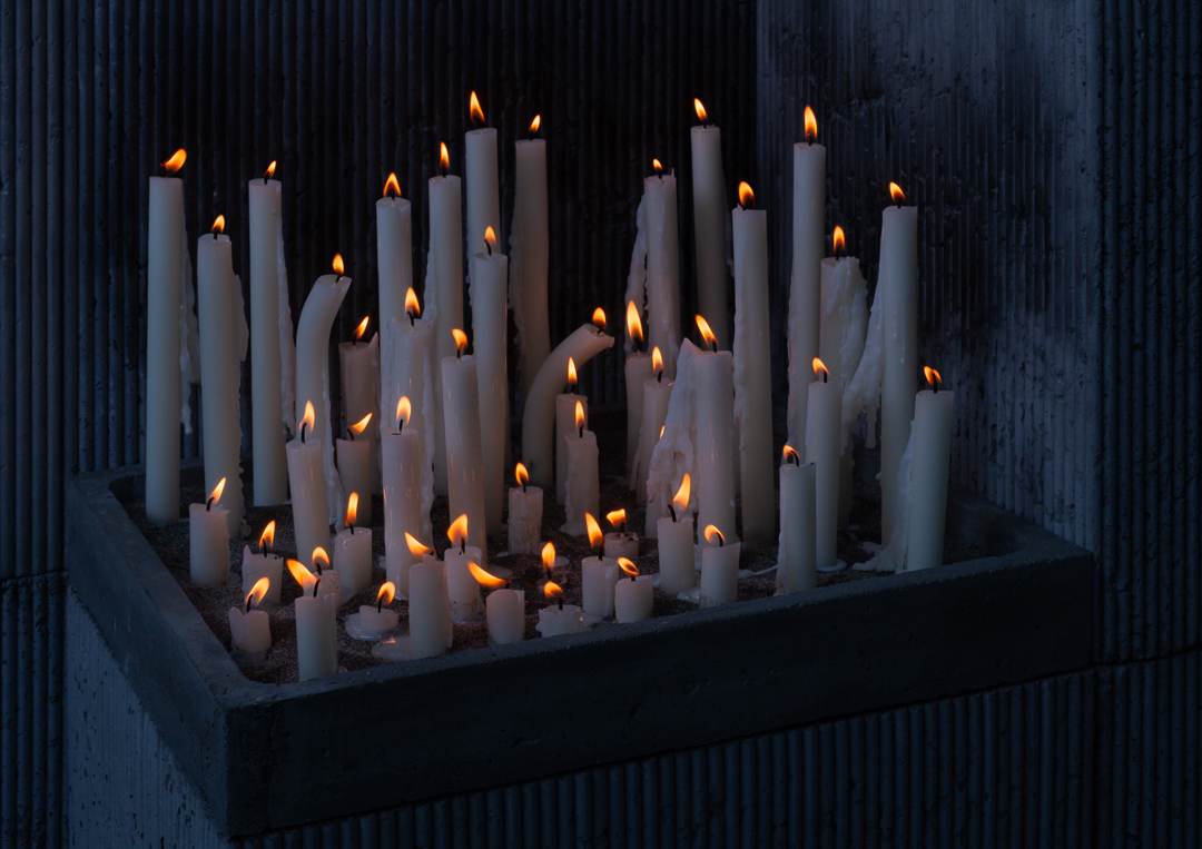 many lit candles in a concrete selling, some of the candles are melting