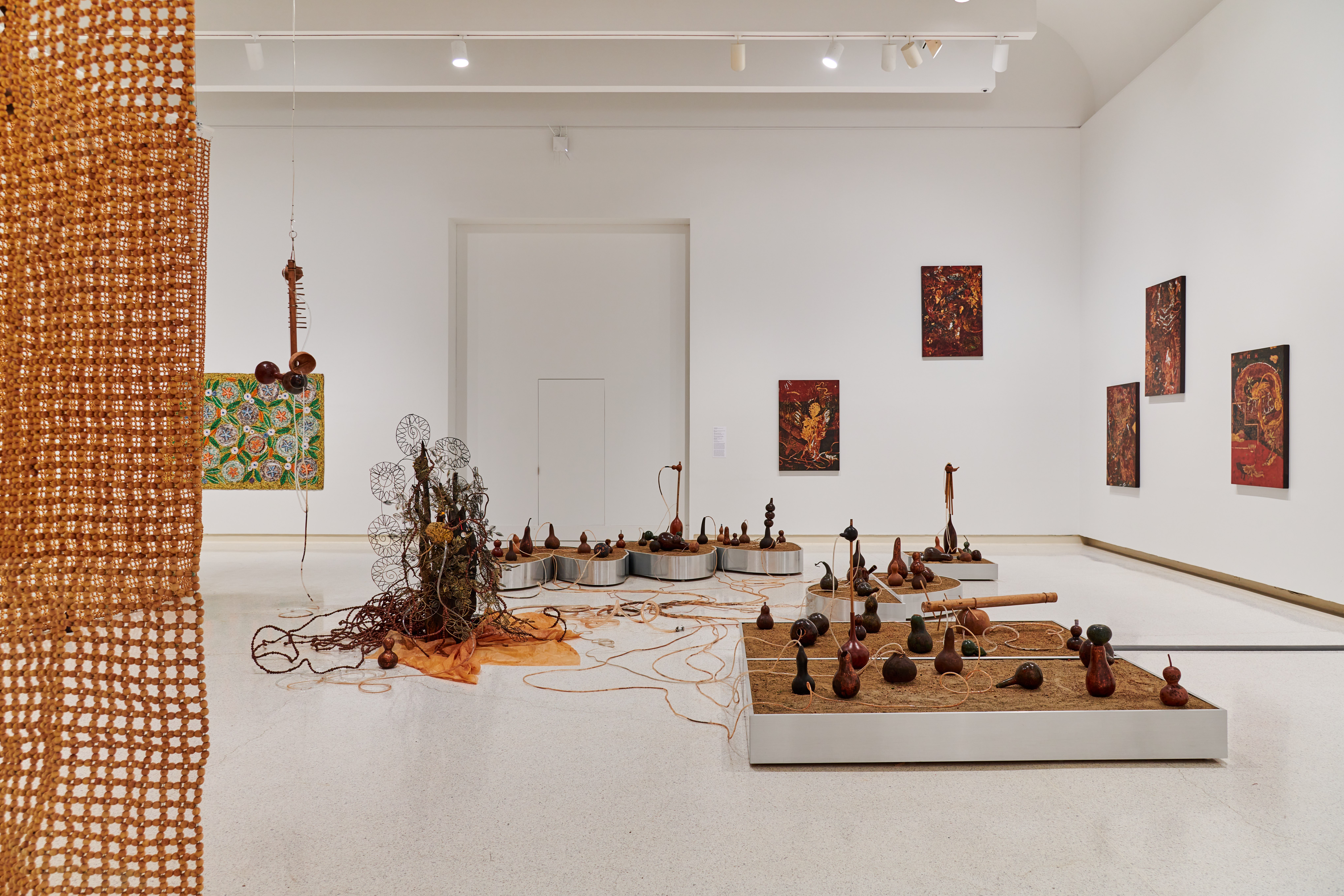 A white wall gallery space that is densely filled with various floor standing sculptures and works hung on the walls.