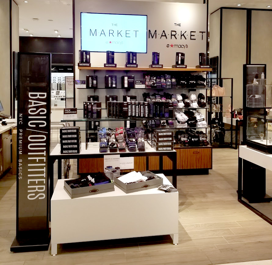 Basic Outfitters clothing package display inside Macy’s Herald Square with a large sign on the logo displayed adjacent to the packaging samples.