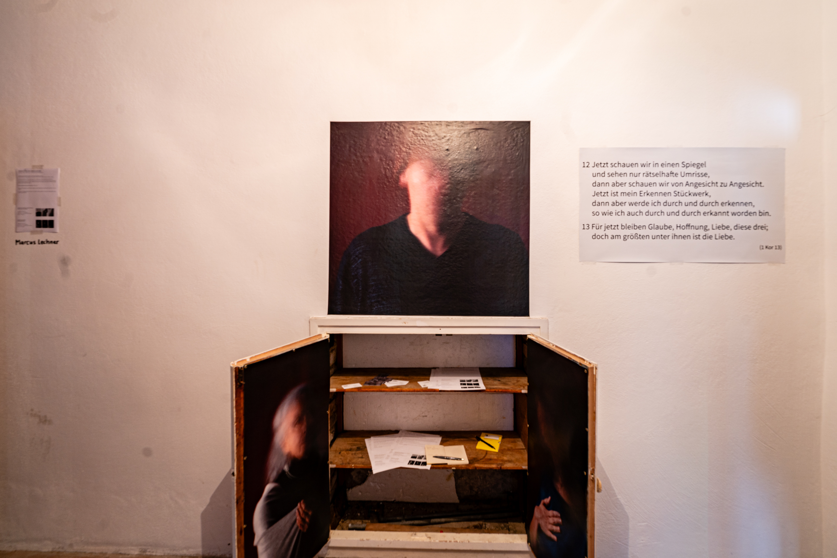 Bild 1 zu Glaube, Liebe, Hoffnung &ndash; Fundament der Resilienz ?: Ein ge&ouml;ffneter h&uuml;fthoher Wandschrank. Auf seinen T&uuml;ren Fotografien von verschwommenen Gesichtern. Dar&uuml;ber ebenfalls eine quadratische Fotografie, die einen Kopf erahnen l&auml;sst.