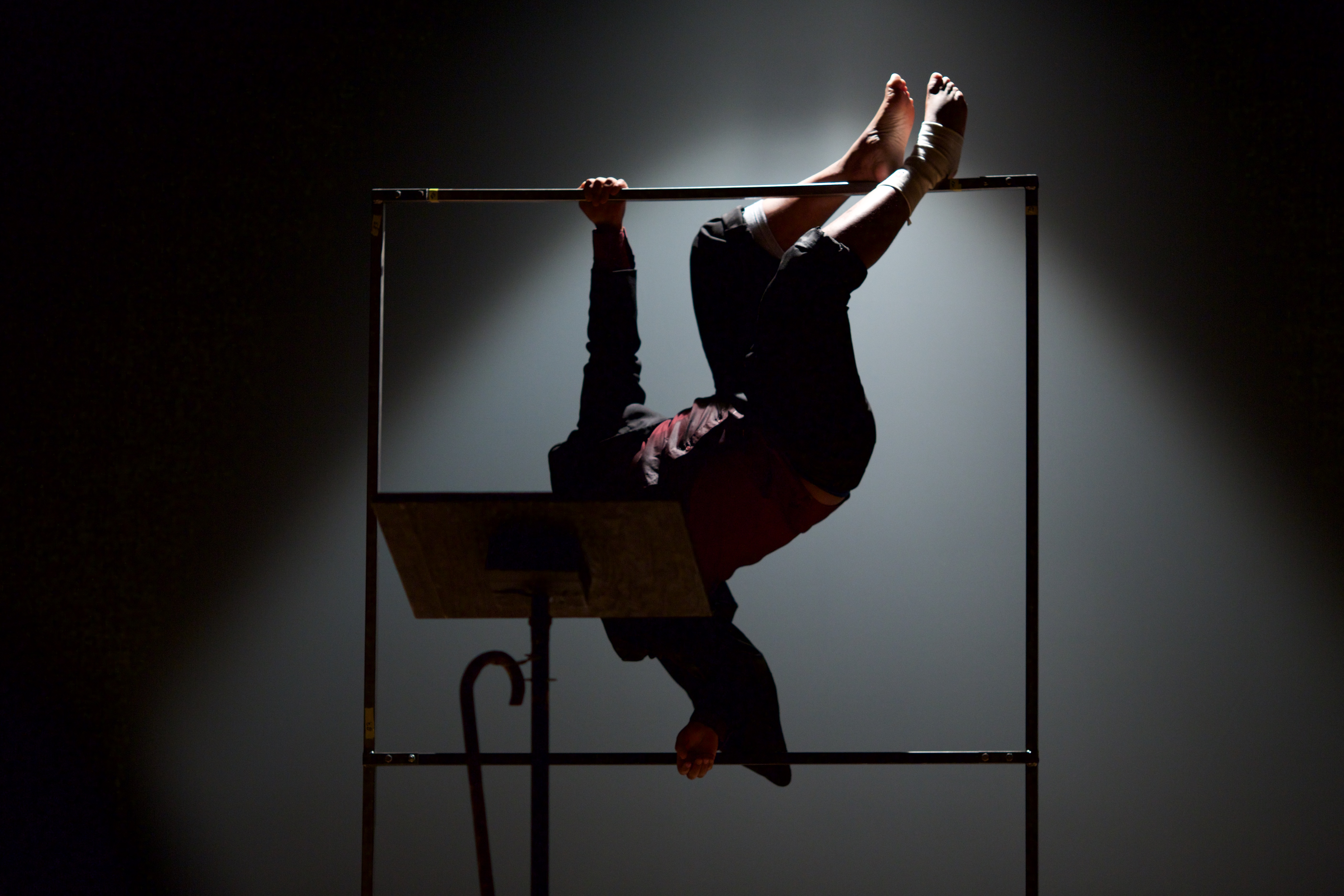 A black man in a suit suspends himself from a frame.