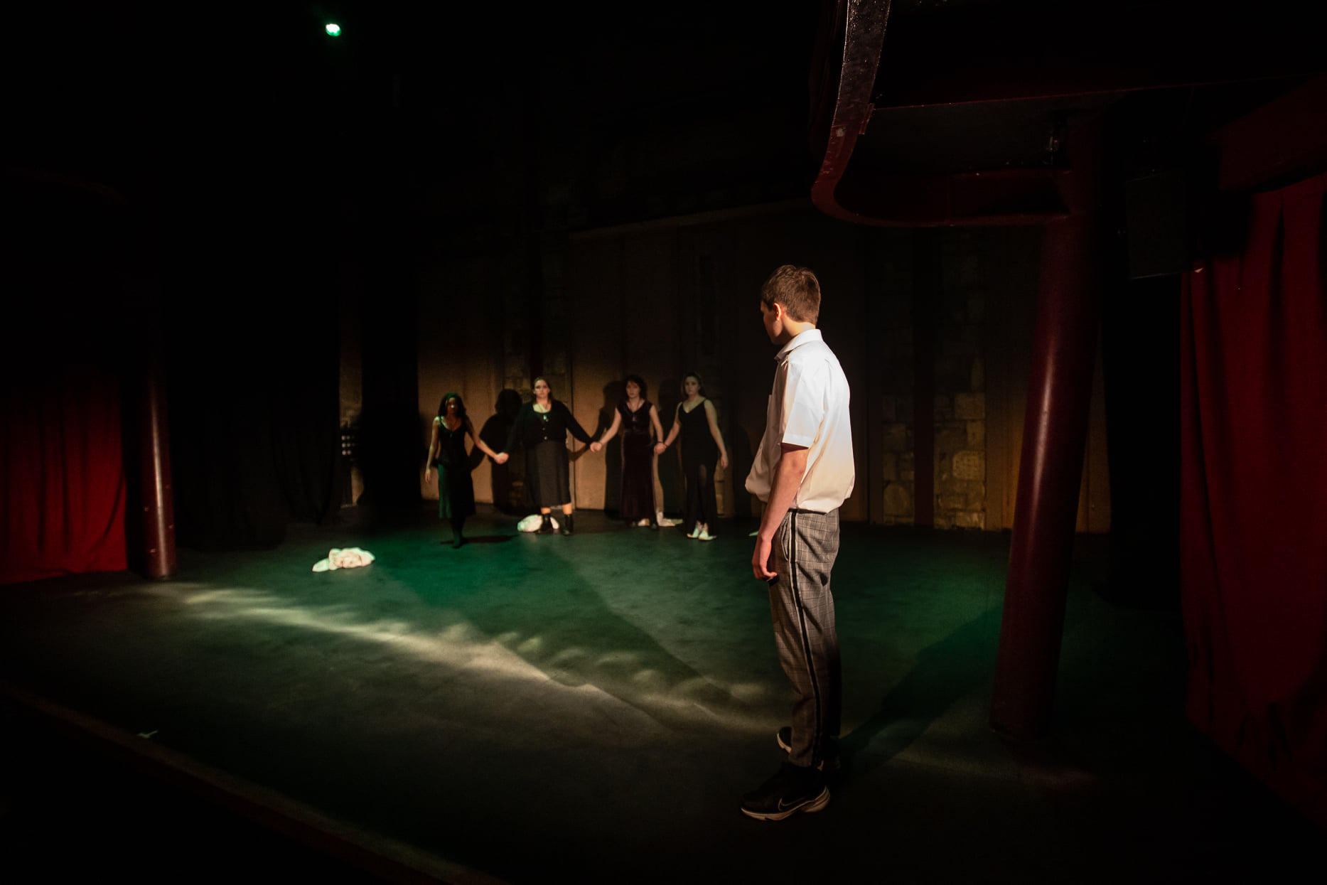 A group of young people huddle at the back of the stage. At the front of the stage, a young man stands behind a line of salt.