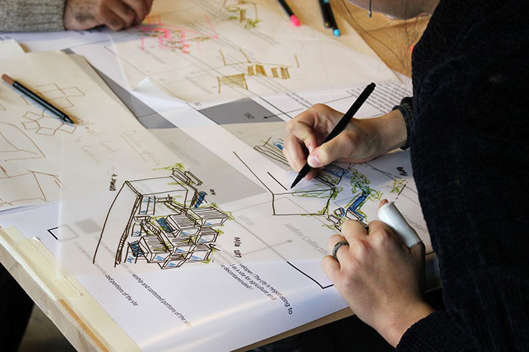 A person holding a pen or pencil working at a drafting table.