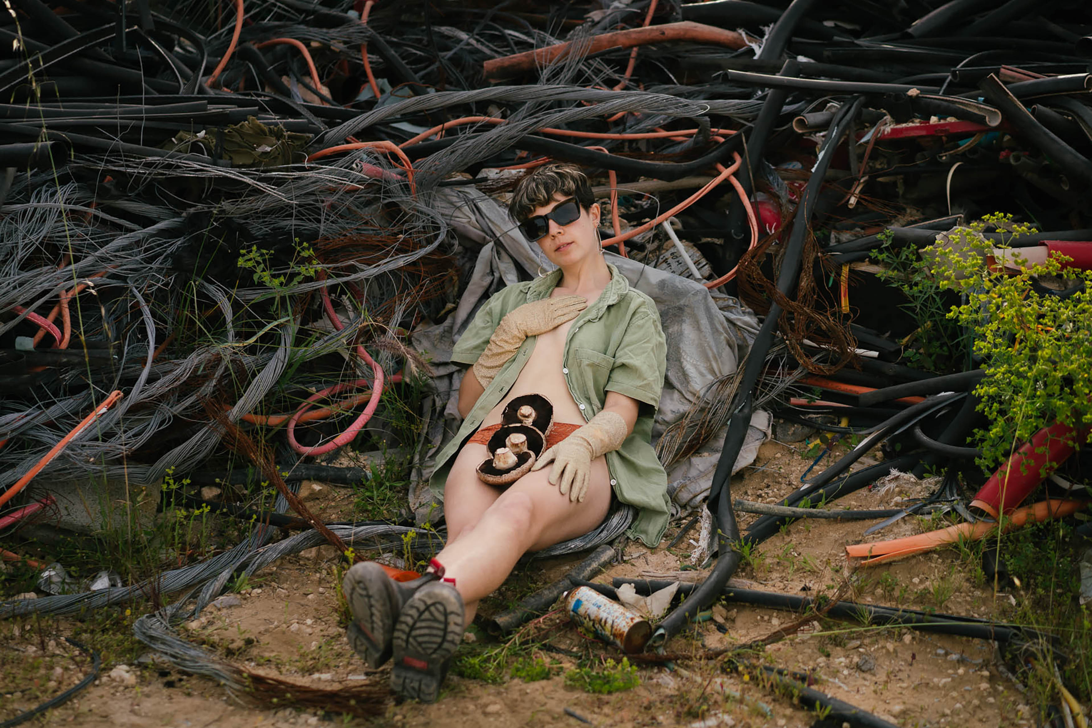 A young person lying in a landfill with mushrooms on their body.
