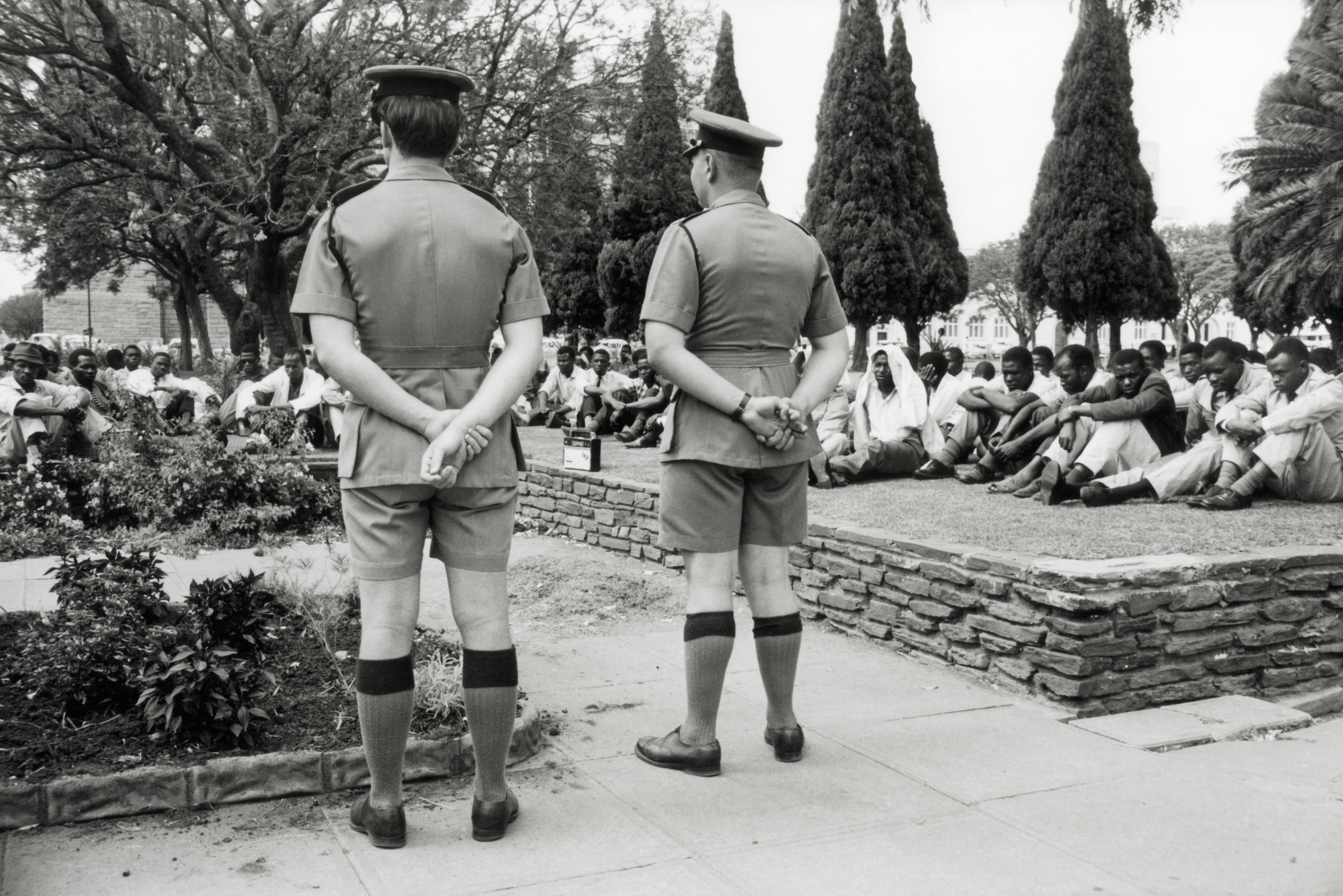Marion Kaplan, 11 November 1965--under the eyes of two policemen, Africans await UDI developments (unilateral declaration of independence) in Salisbury, Rhodesia, now Harare, Zimbabwe, 1965. © Marion Kaplan