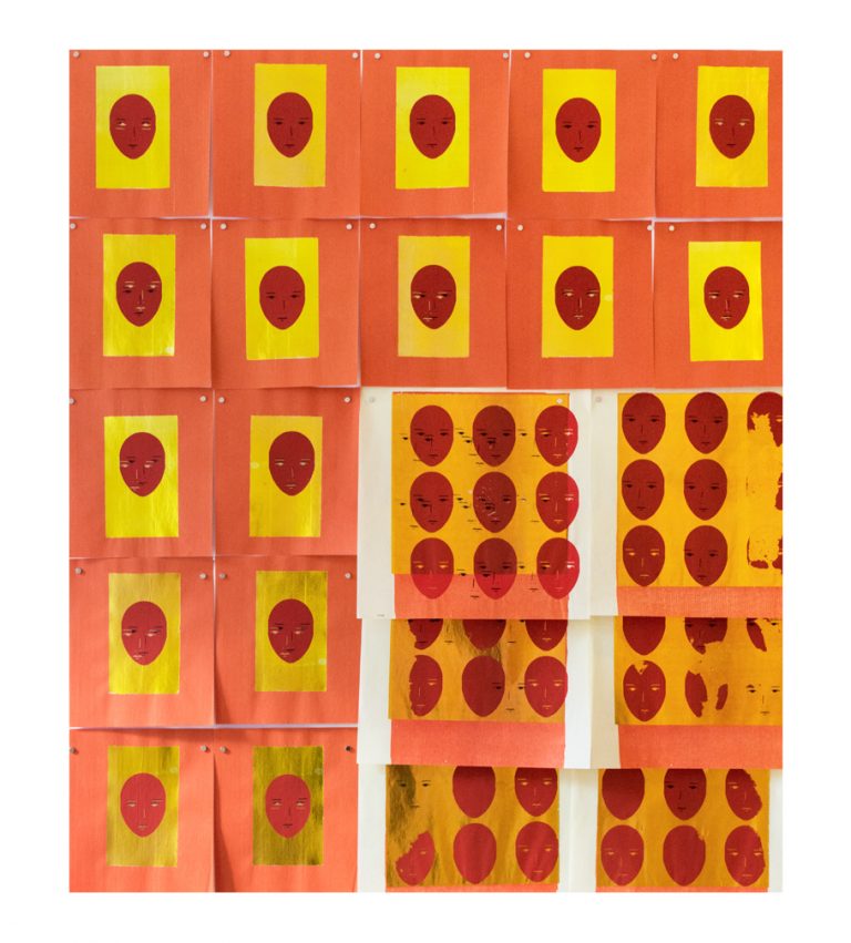 A series of red feminine faces printed on gold paper with a white border. The features on the faces are disorganized, obscured, and appear as if misprinted.  