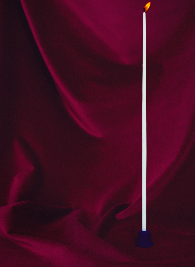burgundy velvet draping with a thin tall candle flame blowing to the right