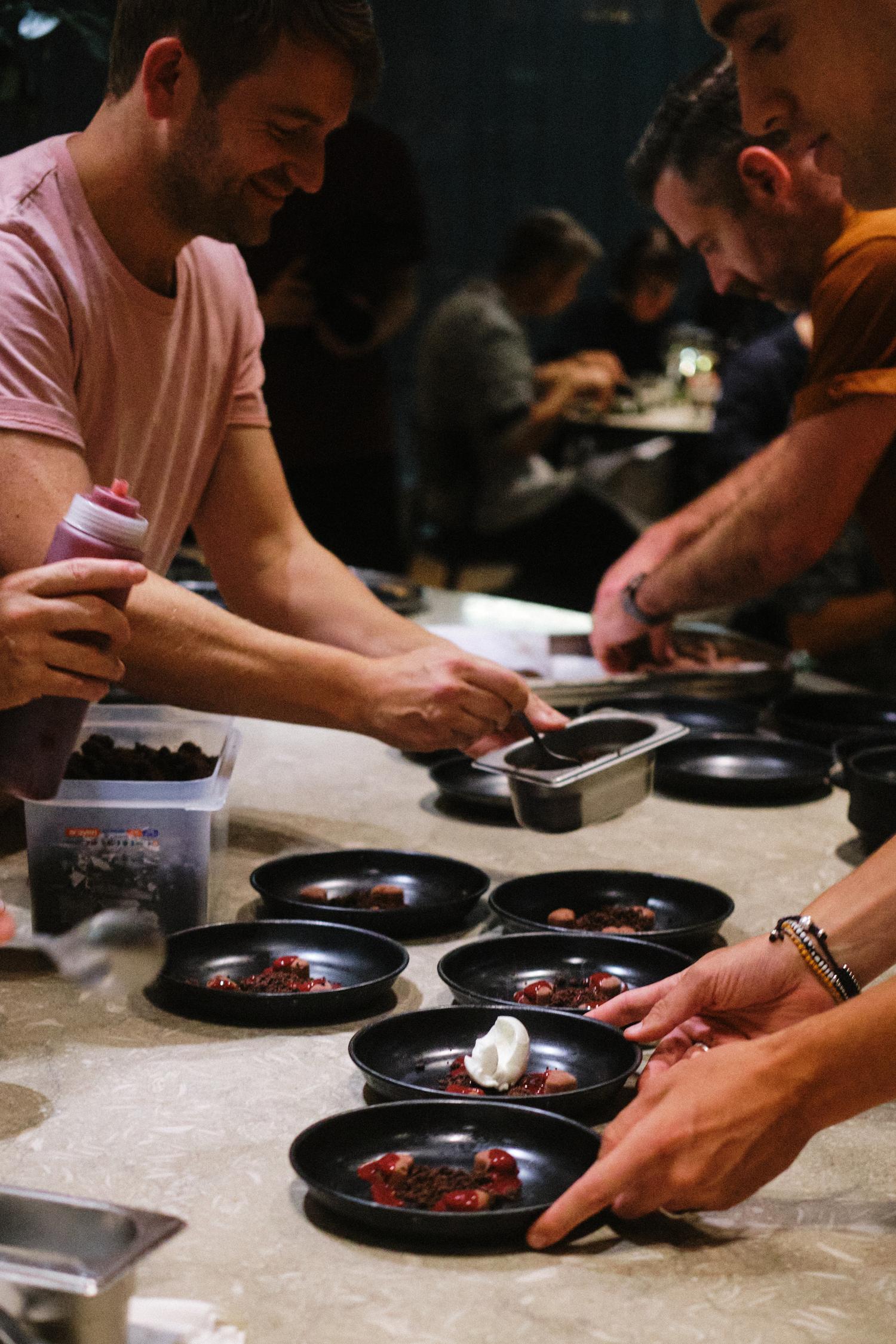 Chefs plating a cherry and chocolate dessert at Paired London inside Carousel, preparing multiple dishes for guests.