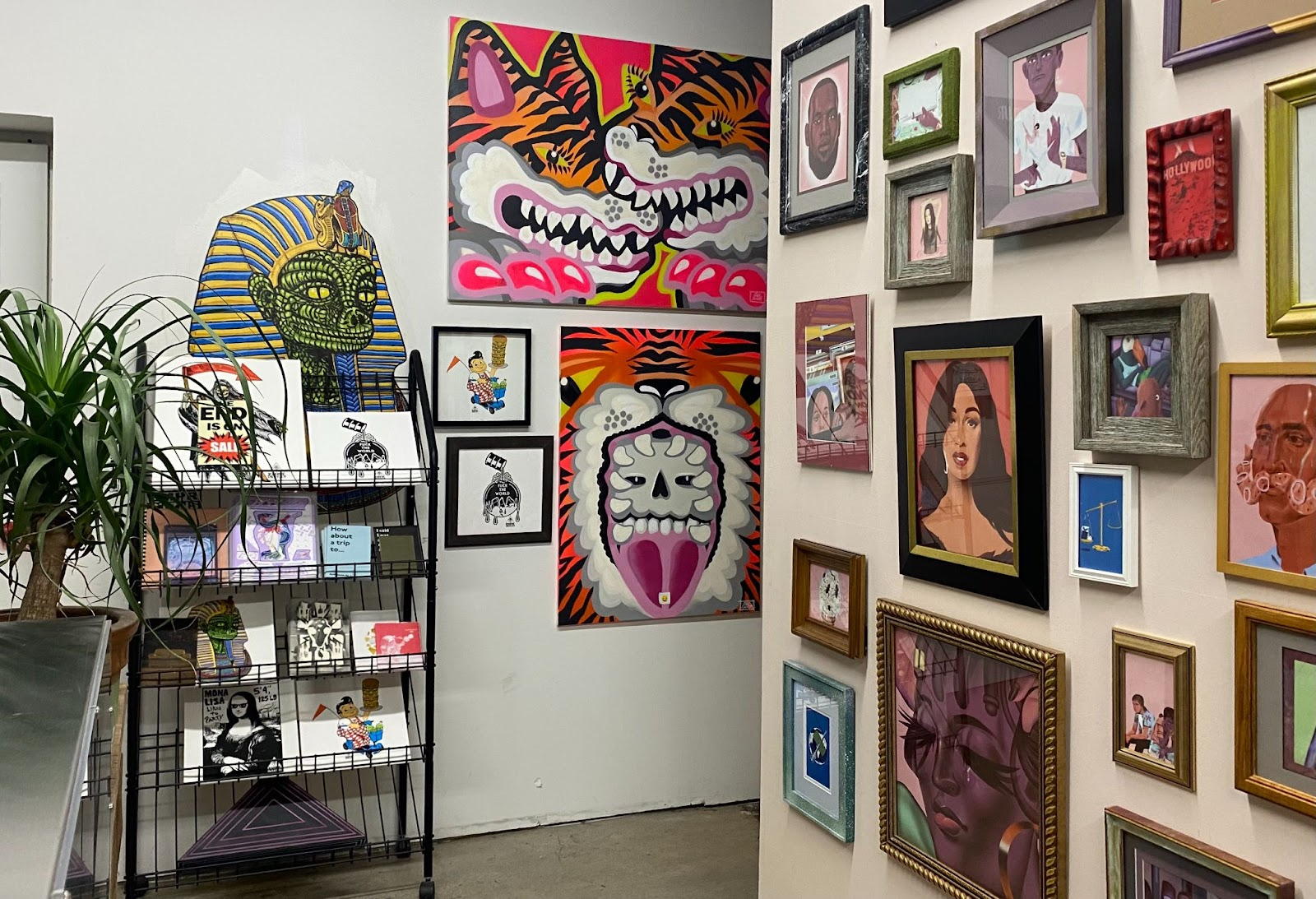 Paintings densely hung on walls in a retail space with carts holding smaller objects and prints.
