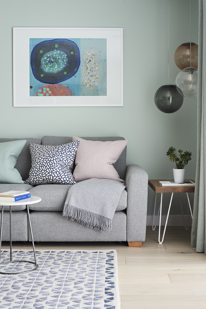 Front perspective of grey sofa. Patterned rug, side tables and abstract framed art on wall. Pink, blue and sea green palette.