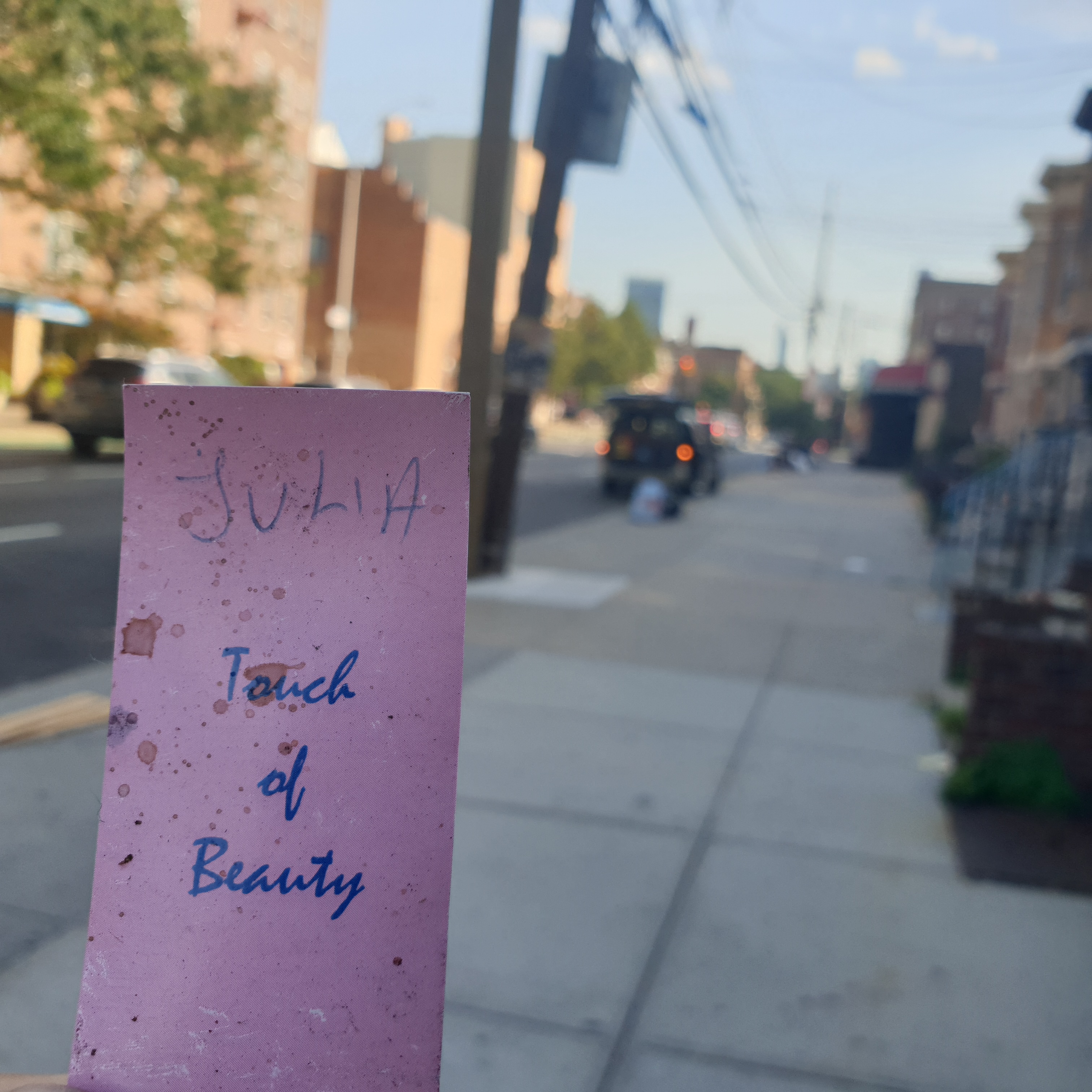 The word Julia handwritten above "Touch of Beauty" on a pink card. A sidewalk is seen in the background.