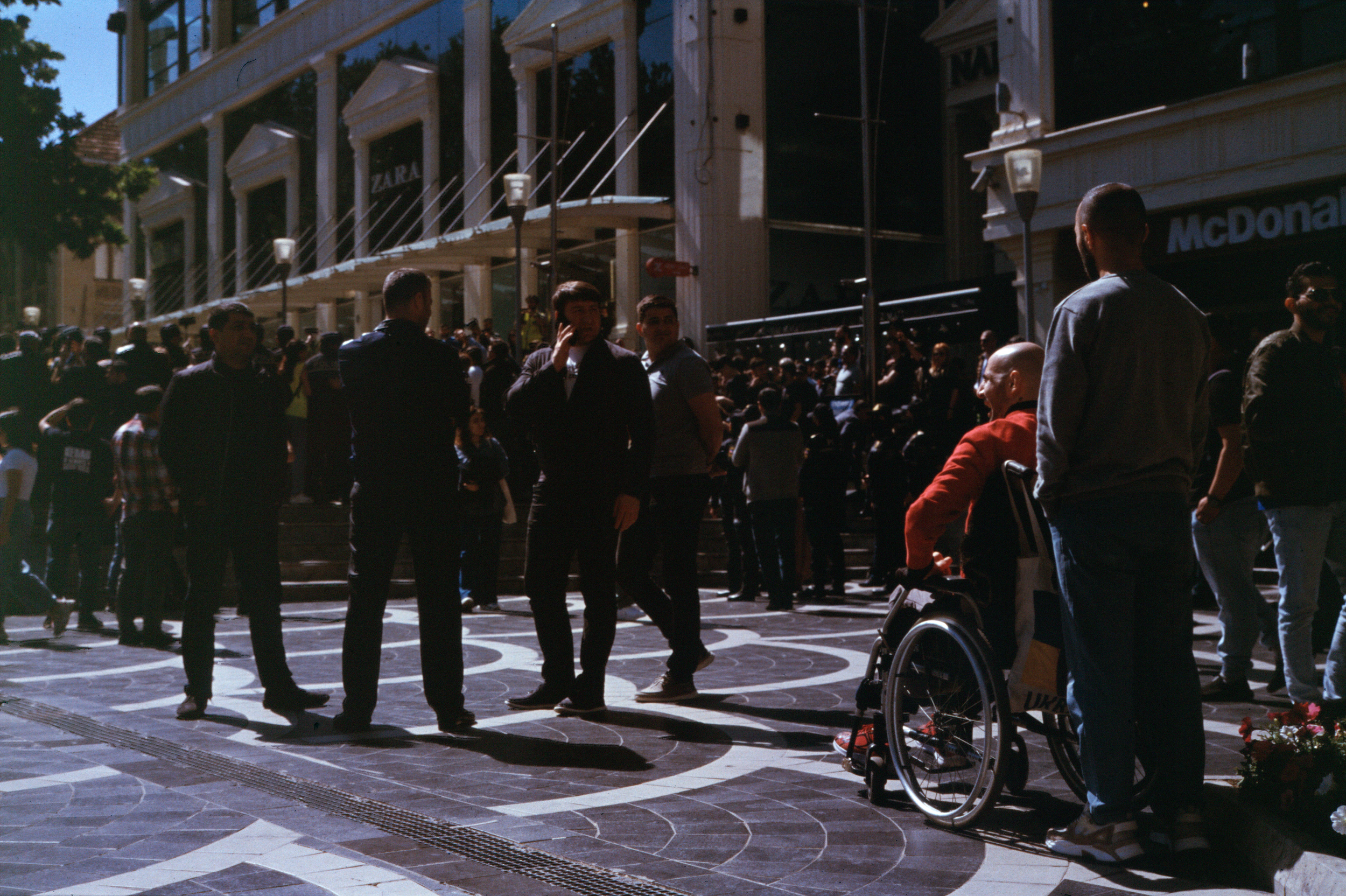 Four men previously seen doing crowd control eye a man in wheelchair demonstrating. Kodak Ektachrome 100.