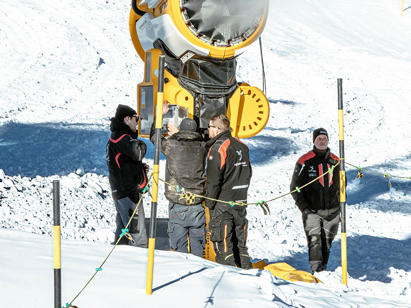 Bergbahnmitarbeitende nehmen eine Schneekanone in Betrieb und stellen den Betrieb sicher.