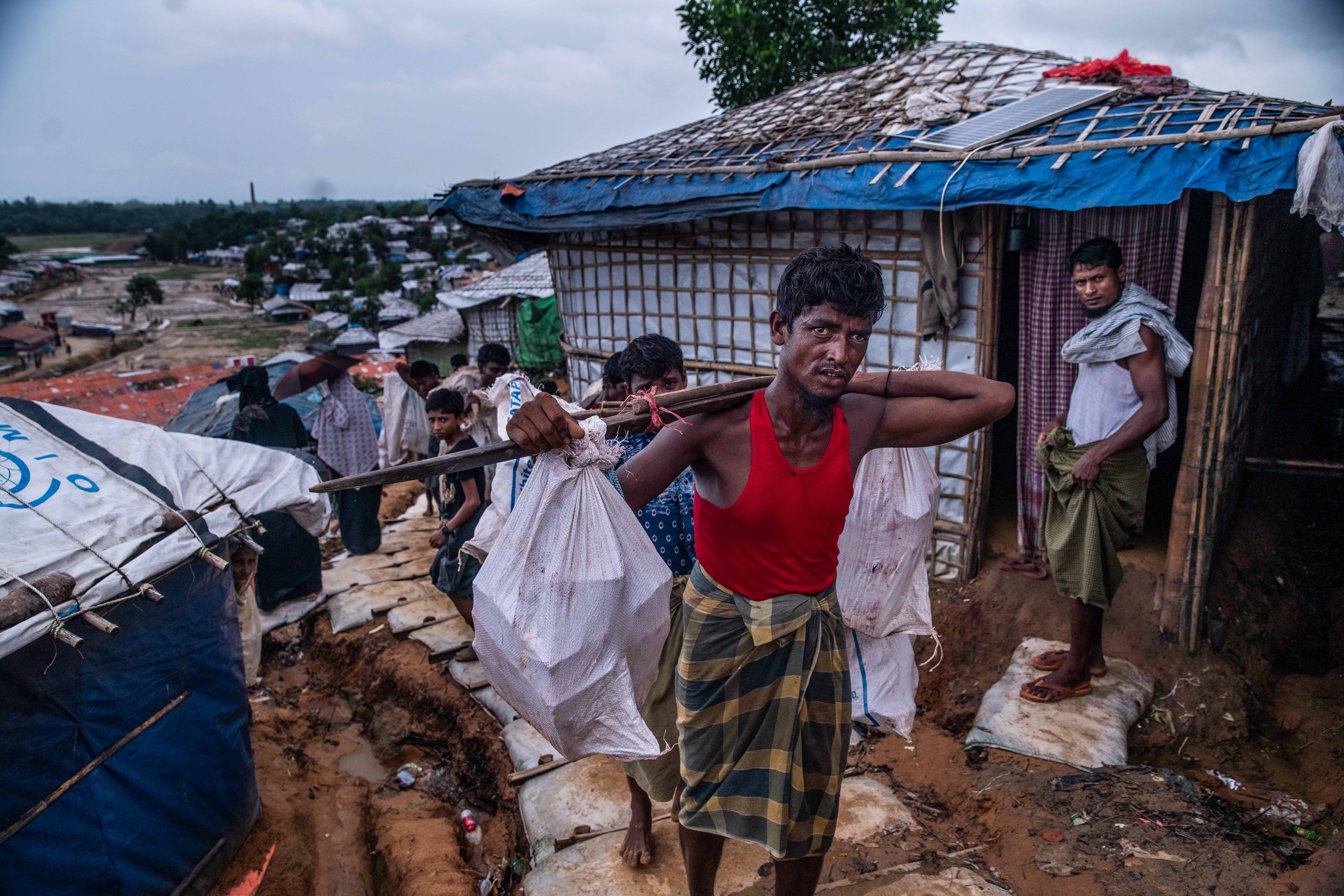 A group of Rohingya men carry supplies back from a nearby distribution center in the Kutupalong-Balukhali expansion site, Cox’s Bazar, Bangladesh on July 29, 2018. Every two weeks, food distribution centers - run by agencies like the World Food Program or the Red Crescent - provide pulses (beans), rice, cooking oil and other rations to registered households. With most employment opportunities in the camps being NGO-funded, daywork and low-income, the majority of Rohingya depend on these provisions to survive. Balukhali camp’s population reaching almost 600,000, one runs into men, women and children carrying provisions such as these every few hundred meters, all day, every day.