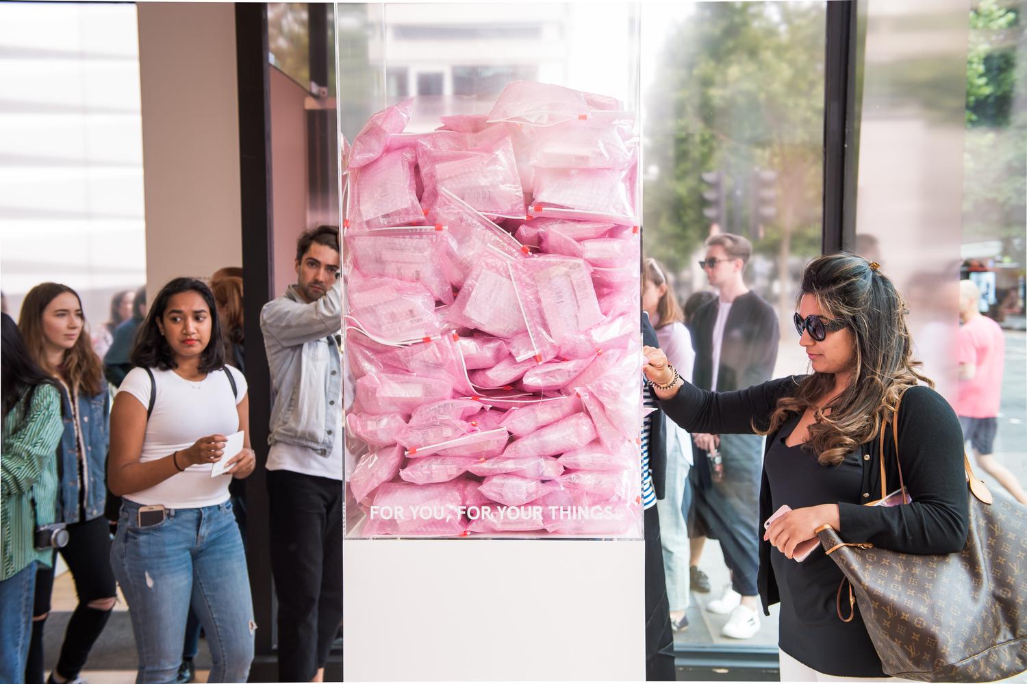 Guests at Glossier London event collecting branded pink gift bags near the entrance.
