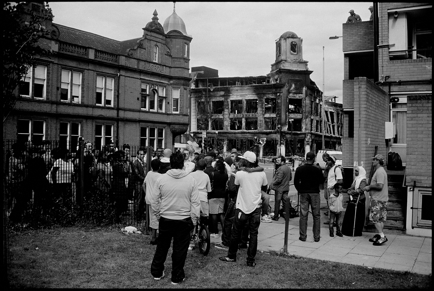 Days after the fatal shooting of Mark Duggan in Tottenham, North London, protestors and news crews gather outside the remains of the landmark CarpetRight building which was burnt down during the riots. August 2011