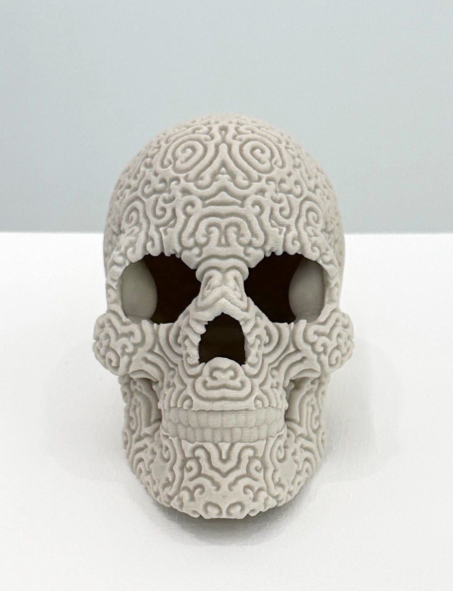 View of a sculpture which is a skull. It appears as though non-figurative, decorative pattern is carved into the surface of the skull.