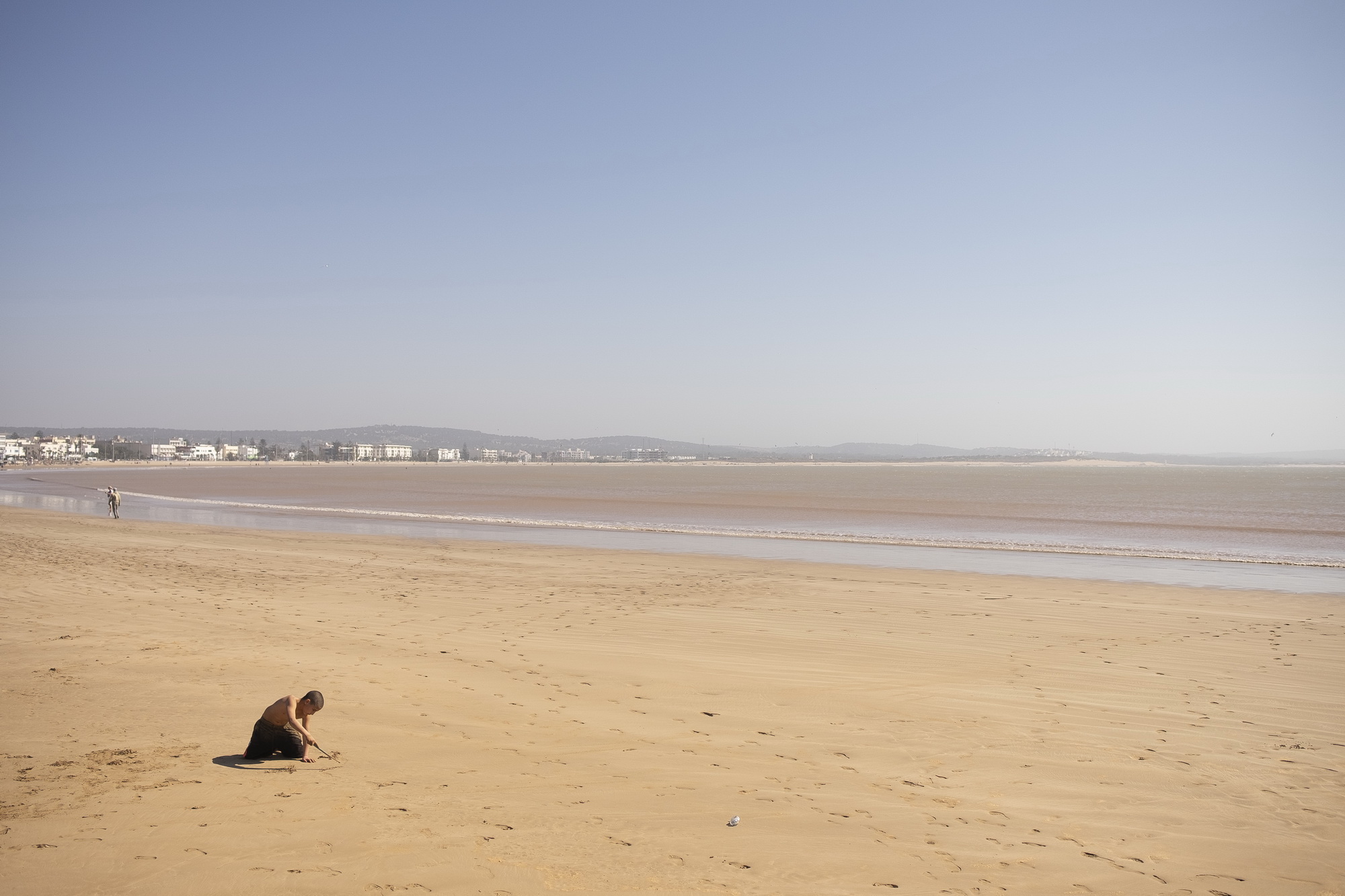 Boy draws in sand on a mostly empty mid-March beach.