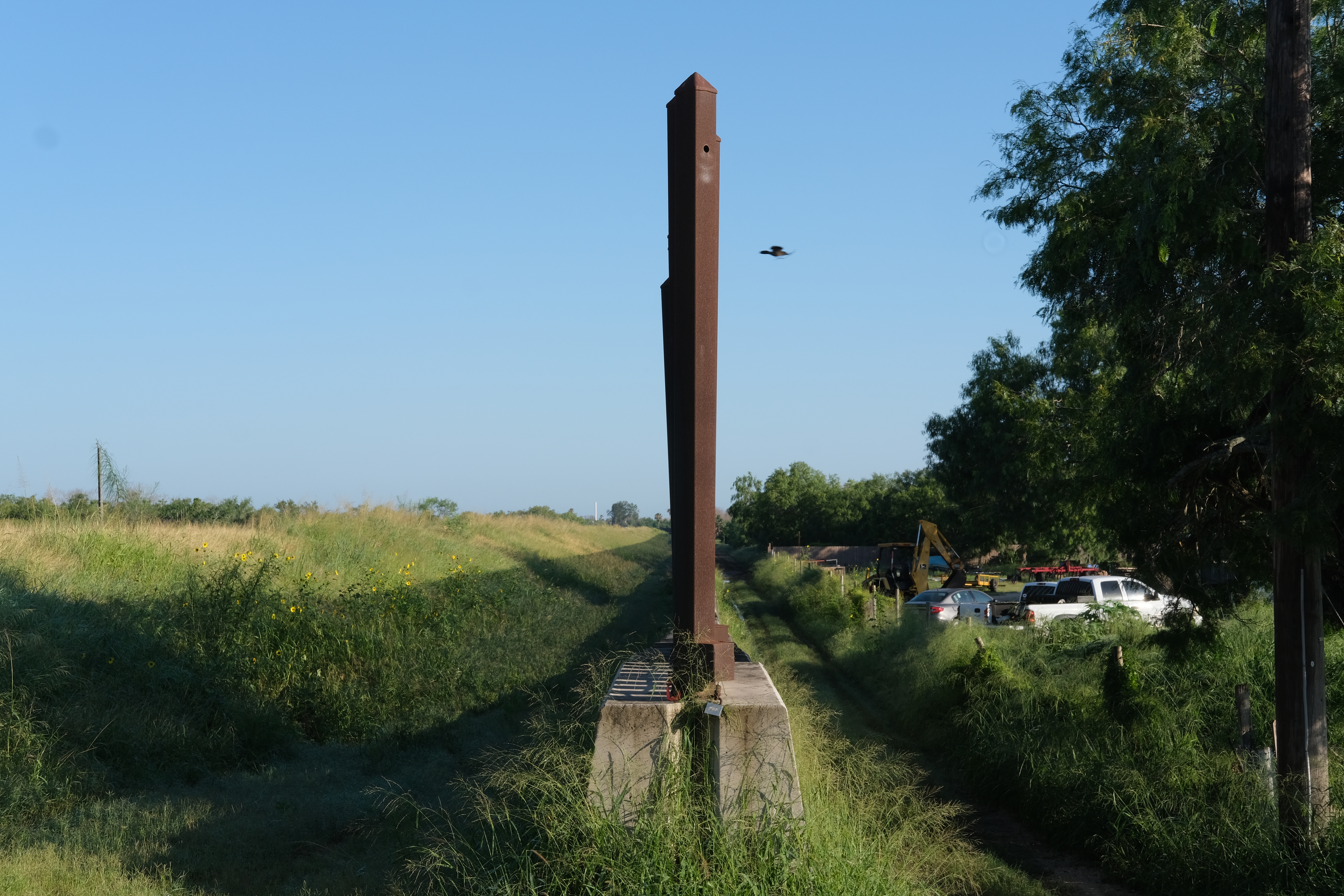 A bird flies over the US-Mexico border wall near Brownsville, TX, which is nearly a mile away from the natural winding border at the Rio Grande. The cutoff sometimes affects farmers living between the river and wall, and also restricts some wildlife from its natural migration.