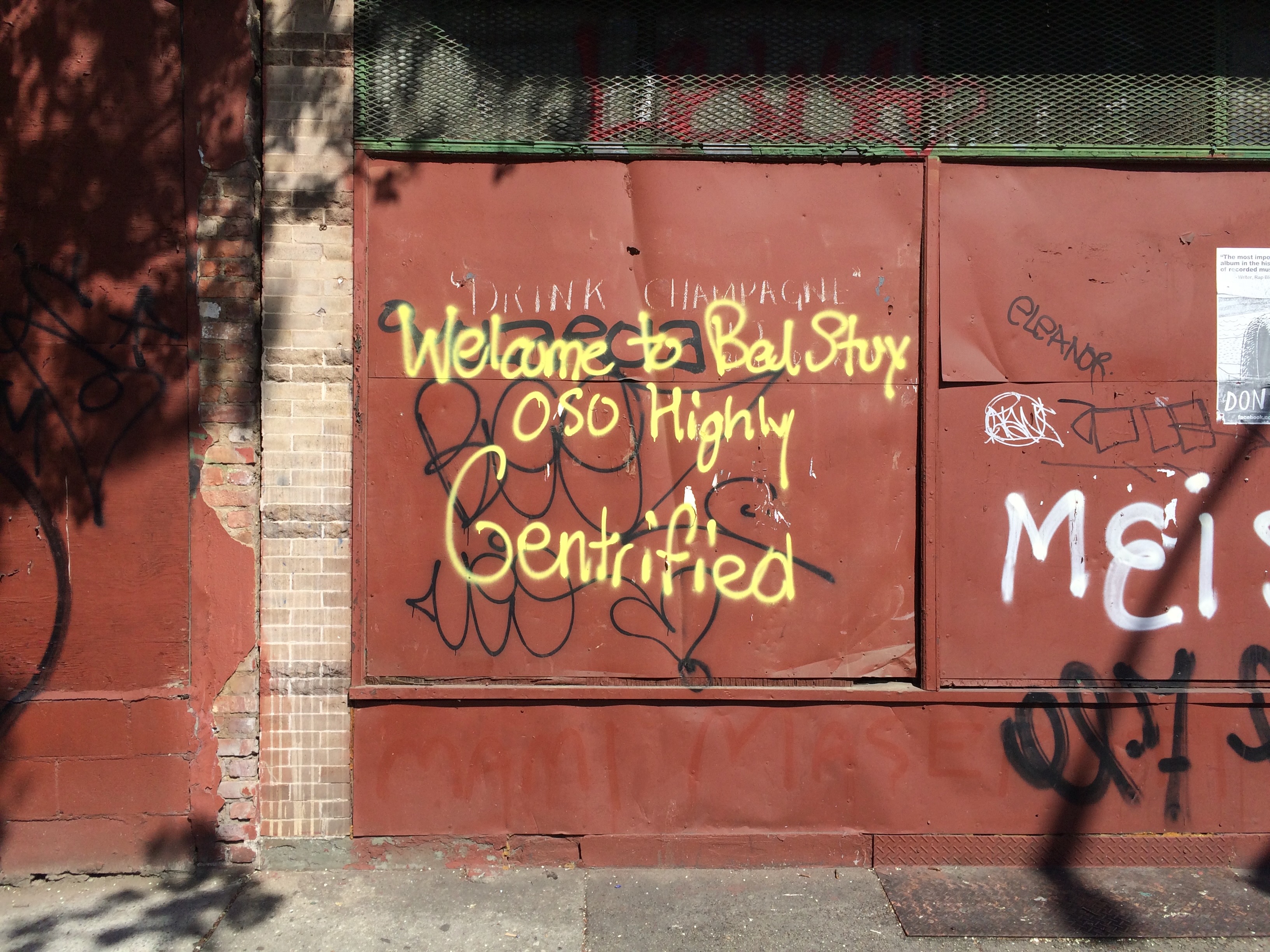 Yellow graffiti on a boarded up building reads: Welcome to BedStuy OSO Highly Gentrified.