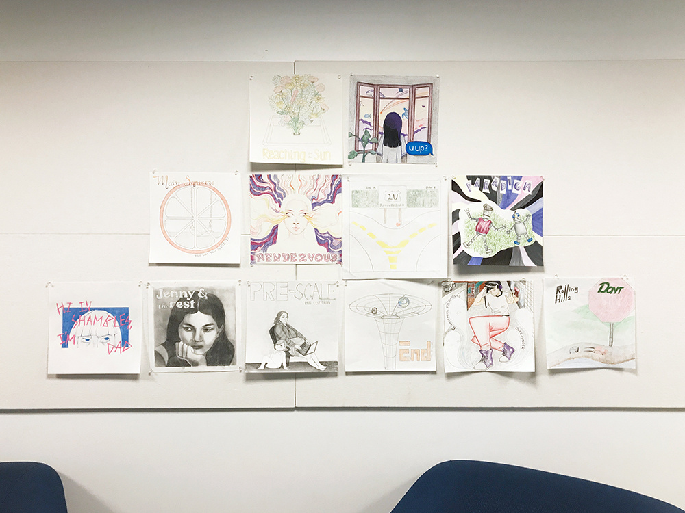 View of 12 artworks in the hallway of an academic building. Various drawings on square-shaped paper are attached to the wall and behind and above two sofas.
