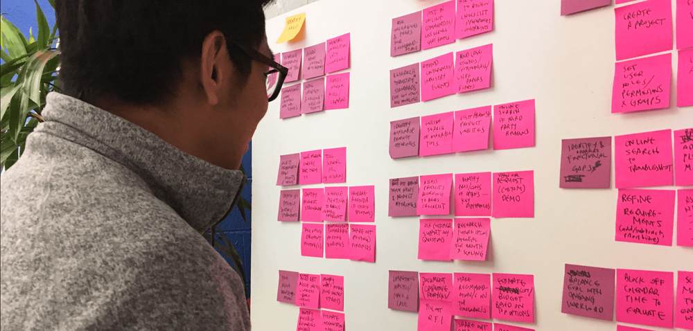 A man wearing glasses looks at a board of post-it notes