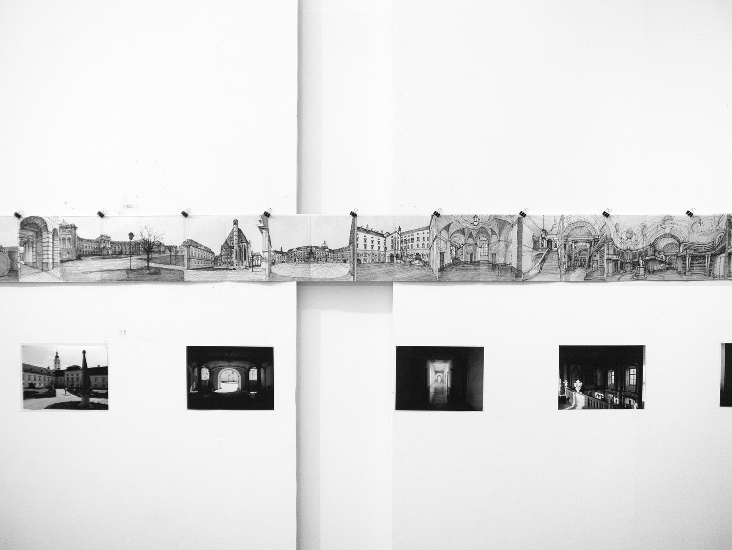 The drawings are strung across tension wires along the walls, coupled with photographs below