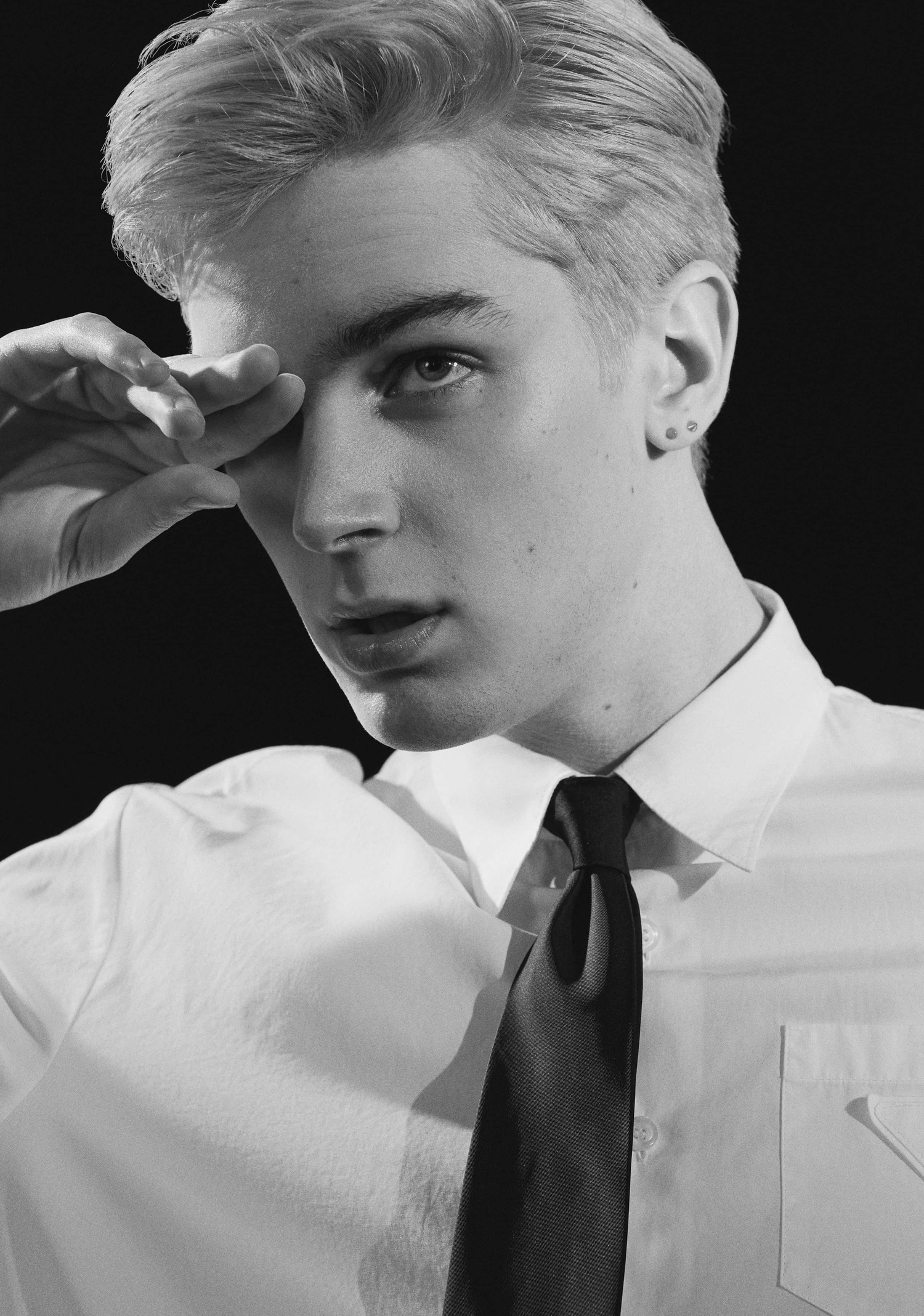 Black and white portrait of male model rubbing his eye, wearing a white Prada button-down shirt and skinny black tie.