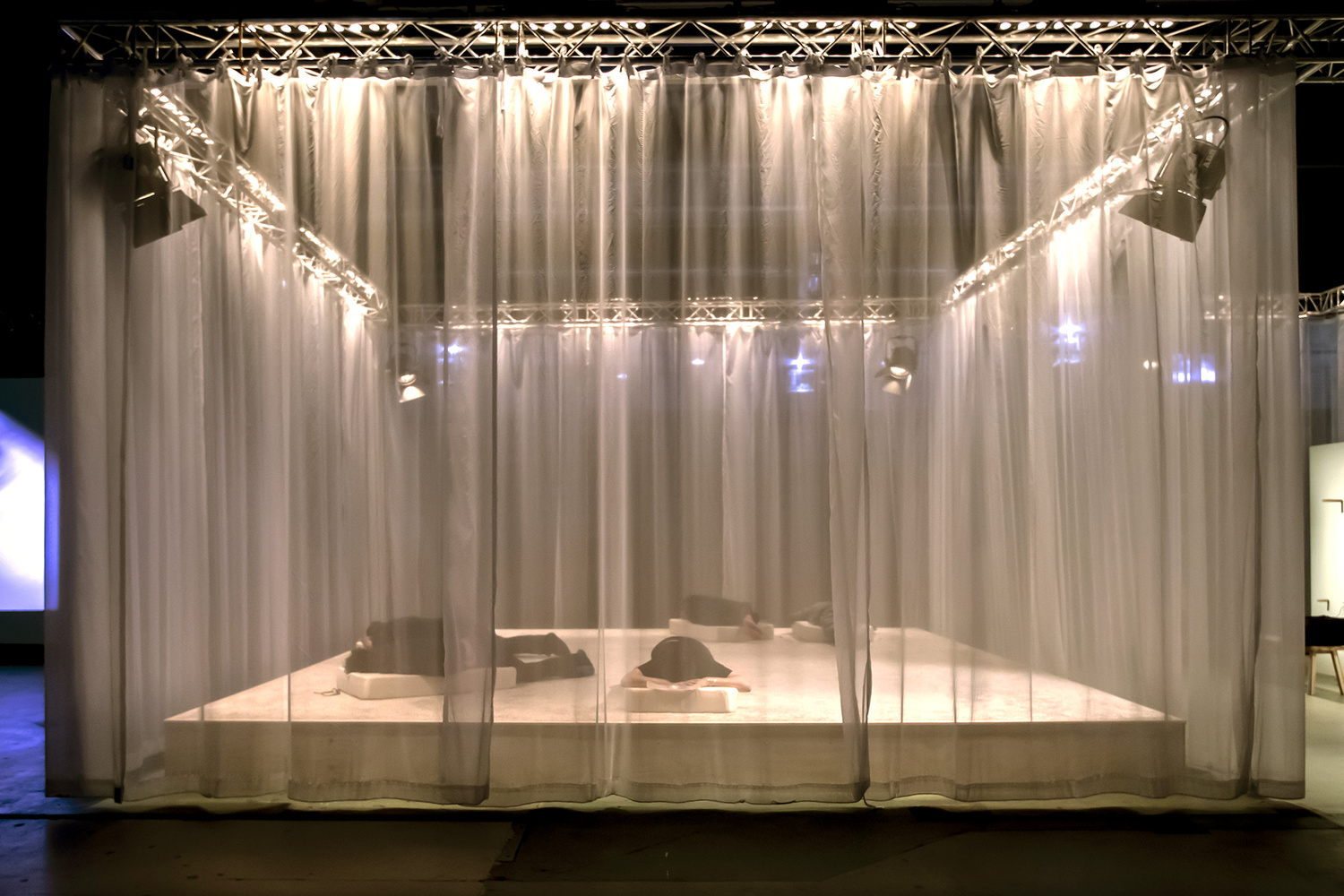 documentation image of the installation from the outside view. the curtains are hanging from a metal structure that surrounds the entire installation. there are five people participating in the installation.