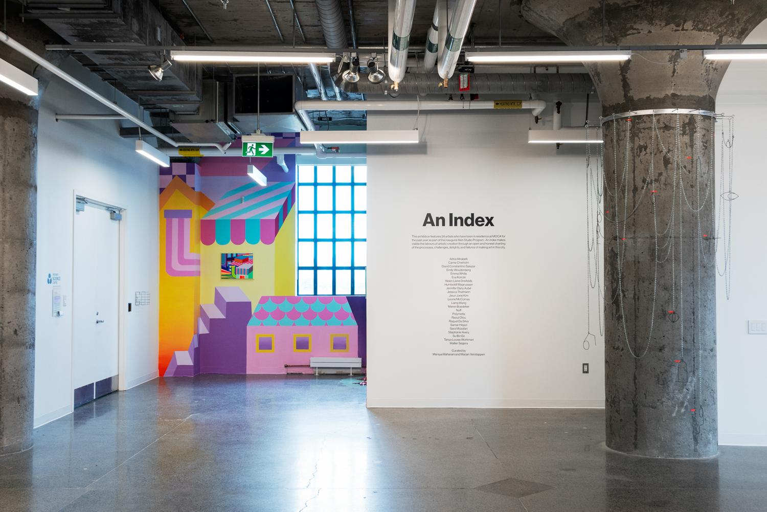 A photo of the start of the exhibition. In the middle of the image, a black vinyl text on a white wall lists the exhibition title and statement, as well as credits the artists and curators. On the left side of the image, a mural by Kim of a colourful dream world that animates a nook in the gallery with a large paned widow. On the right side of the image, a grey structural column is draped with an aluminum chainlinnk site-specific scupture.