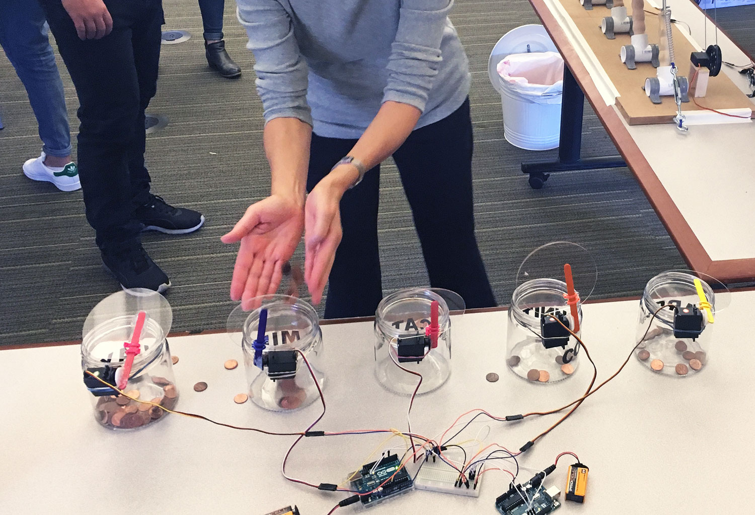 A person emptying coins into one of five jars, each of which is connected to electronics