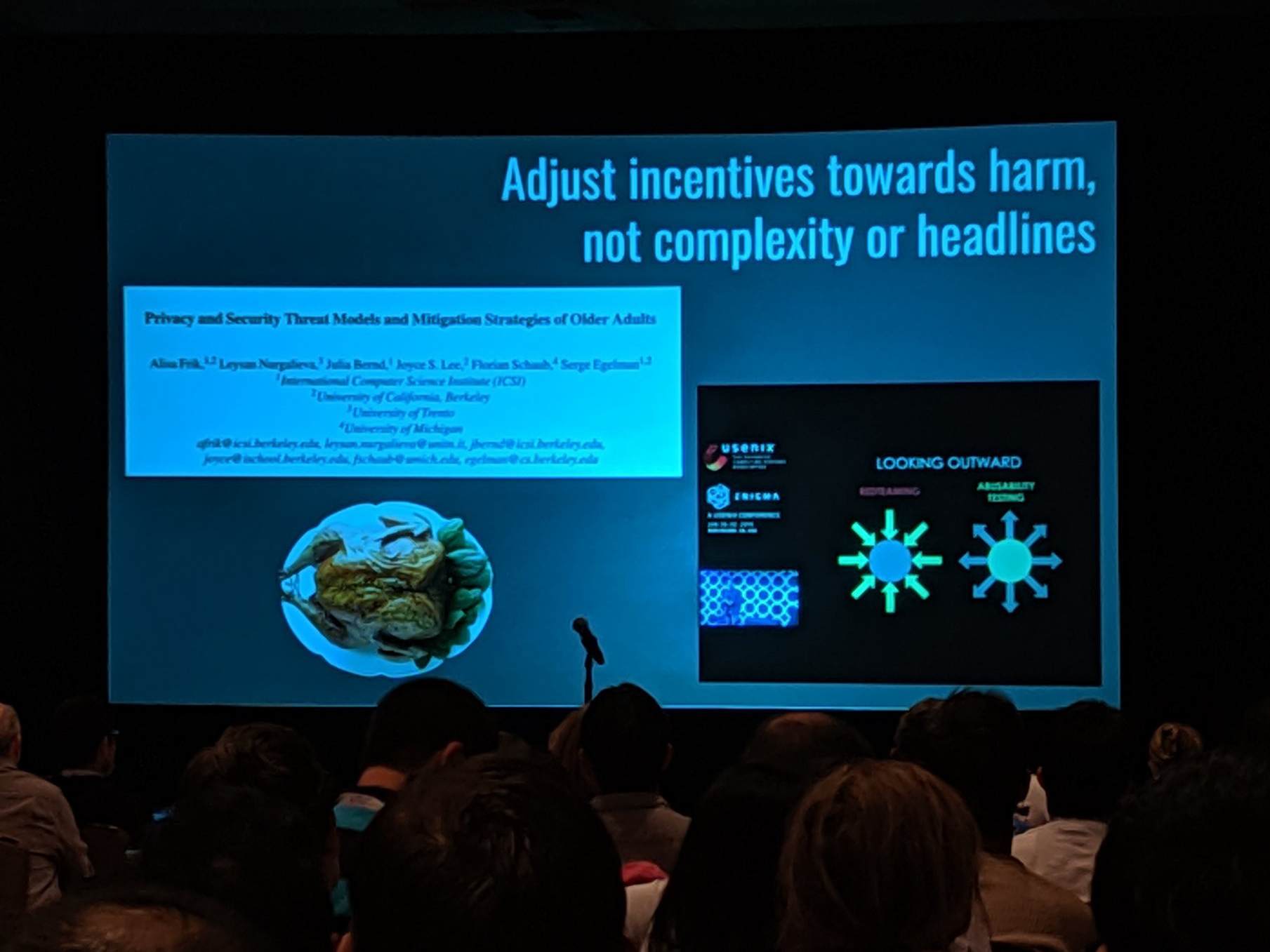A slide projected in a dark room in front of a crowd. The slide reads 'Adjust incentives toward harm, not complexity or headlines'