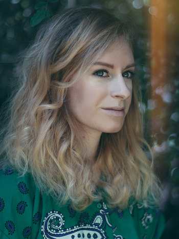 Laurel outside wearing a green blouse with a paisley pattern, in front of blurry trees 