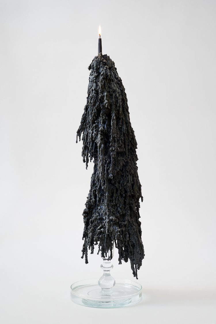 An image of a lit black candle atop a baroque column of black dripped wax. The column is supported by a glass candlestick standing in a large glass Petri dish filled with water.  For Release is the physical artifact of a ritual Margaux Crump performed to release her fears.
