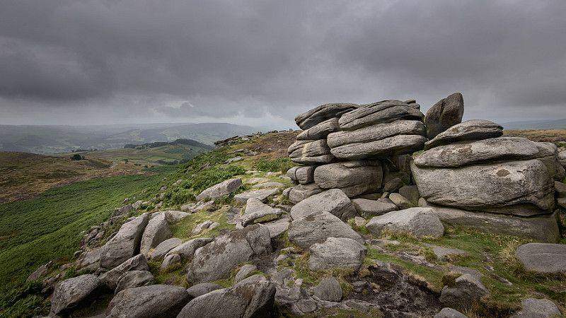 View of a natural landscape of rocks nearby, hills continued afar, and dark clouds right above.