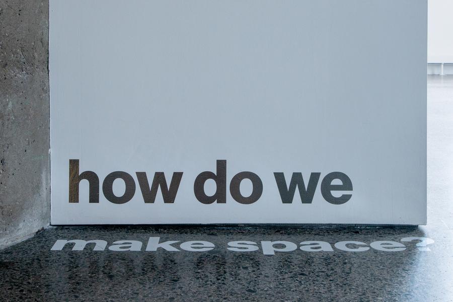 As the white wall meets the grey floor, a silvery vinyl text reads across the two surfaces, quote, how do we make space?, end quote.